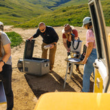 Group of people preparing for an outdoor adventure with a Dometic CFX5 35L Portable Fridge, in a natural setting.