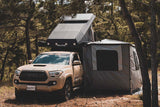 Alu-Cab 270 awning, with the Awning Side Wall Kit and a hard shell rooftop tent, fitted to a camping vehicle in the forest 