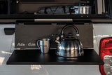 Stainless steel kettle and mug on a black Alu-Cab Side Slide Prep Table on a white Camp4x4 vehicle