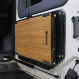 Wooden table top of the Alu-Cab INEOS Drop Down Table Mounting Kit on a vehicle door with black frame