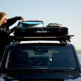 A Camp4x4 rental vehicle, fitted with the Alu-Cab LT-50 Lightweight rooftop tent, with a person securing surfboards to the roof