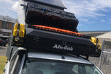 An offroad Camping vehicle fitted with an Alu-Cab Gen3.R rooftop tent, and the Alu-Cab Roof Box. A sturdy aluminum storage box fitted with the Alu-Cab Jerry can Holder