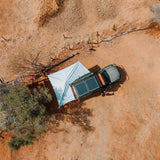 Aerial view of a car with an extended Alu-Cab 270 Shadow Awning,  solar panels on its roof parked in a desert landscape. Camp4x4. overlanding, camping. Double Cab. Single Cab. Extra Cab