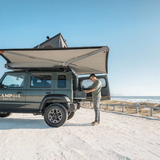 Man setting up an Alu-Cab 270 Awning and Hard shell rooftop tent on a Jimny 4x4 by the beach