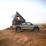 camp4x4.co.za Someone sitting in an Alu-Cab Gen3-R Hardshell Rooftop Tent, mounted to a double cab bukkie, in a dry landscape