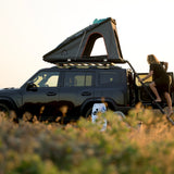 A Camp4x4 rental vehicle, fitted with the Alu-Cab LT-50 Lightweight rooftop tent. A person is climbing the ladder into the tent, in a grassland eviroment