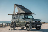 Camp4x4 Suzuki Jimny in dark olive green colour with a ladder leading to a rooftop tent on a beach