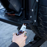Alu-cab can crusher mounted onto the spare wheel of a 4x4 spare wheel, with someone using the bottle opener