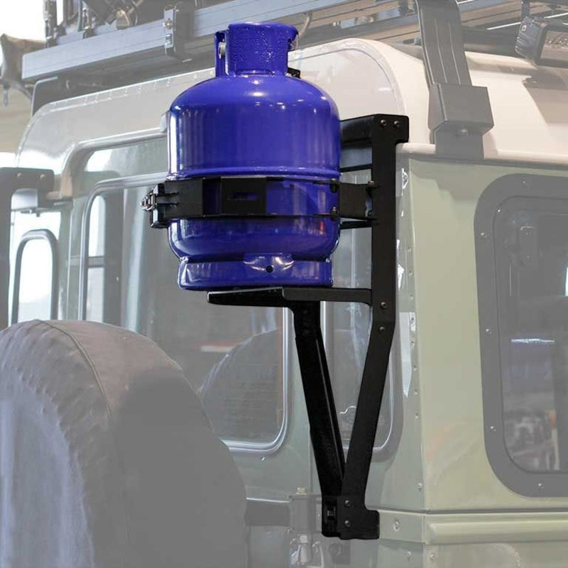 A blue gas tank mounted on a Front Runner Land Rover Defender 90/110 Single Gas Bottle Bracket attached to the gutter of a light-colored vehicle.