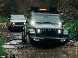 Two off-road vehicles navigating a muddy trail in a forested area with a Front Runner Jeep Wrangler JL 4 Door (2018-Current) Slimline II 1/2 Roof Rack Kit  on 