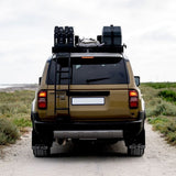 Back view of a beige SUV with Front Runner roof rack and accessories on a dirt road.