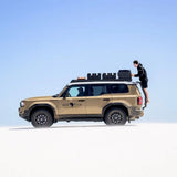 Beige Toyota Land Cruiser Prado 250 with roof Front Runner Roof Rack and 'Will Africa' branding on a clear blue sky background