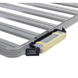 A close-up of a gray metal roof rack crossbar system with a Front Runner Series 10" LED Light Bar VX250-FL Mounting Bracket, shown on a white background.