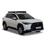 A white Toyota SUV with a black Front Runner Toyota Corolla Cross (2020-Current) Slimline II Roof Rack Kit, shown from a three-quarter front angle on a clean white background.
