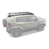 A black Front Runner Toyota Land Cruiser FJ (2026-Current) Slimsport Roof Rack Kit mounted on the roof of a beige SUV, shown from a three-quarters rear angle against a white background.