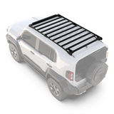 A black Front Runner Toyota Land Cruiser FJ (2026-Current) Slimsport Roof Rack Kit / Light Bar Ready mounted on the roof of a white SUV, shown from an elevated rear three-quarter angle on a light gray background.