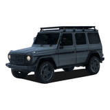 A Mercedes-Benz G-Class SUV with a Front Runner Series Mercedes-Benz Gelandewagen G Class (1979-2017) Slimline II Roof Rack Kit, black wheels, and off-road tires, shown from a three-quarter front angle on a white background.