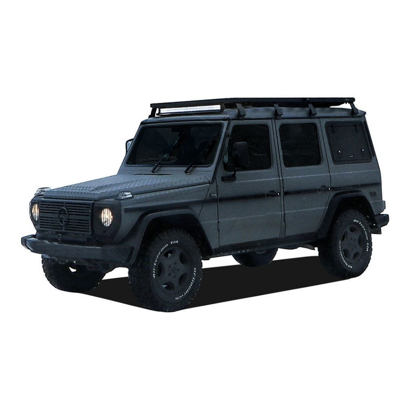 A Mercedes-Benz G-Class SUV with a Front Runner Series Mercedes-Benz Gelandewagen G Class (1979-2017) Slimline II Roof Rack Kit, black wheels, and off-road tires, shown from a three-quarter front angle on a white background.