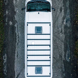 A top-down aerial view of a white recreational vehicle or camper with a Front Runner Toyota HiAce LWB (2019-Current) Slimpro Roof Rack Kit, parked on a cracked asphalt road.