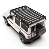 A black Front Runner Ineos Grenadier (2022-Current) Slimline II Roof Rack Kit cargo carrier mounted on the roof of a white SUV, shown from a high-angle rear three-quarter view on a white background.