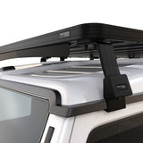 A close up view of a Front Runner Ineos Grenadier (2022-Current) Slimline II Roof Rack Kit, mounted to the roof of a white vehicle, with a black mounting bracket and a small visible FRONT RUNNER brand label.