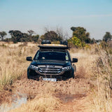 An off-road Isuzu vehicle fitted with a Front Runner Series Isuzu MU-X (2021-Current) Slimline II Roof Rack Kit, with accessories attached to the rack, in the bush