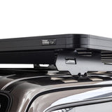 Close-up of a Front Runner Suzuki Jimny (1998-2018) Slimline II Roof Rack Kit mouinted to a vehicle roof, with visible Front Runner branding on the hardware and a small badge on the crossbar.