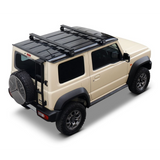 A beige Suzuki Jimny SUV with a blackFront Runner Suzuki Jimny (2018-Current) Load Bar Kit and black trim, shown from a three-quarters rear angle on a white background.