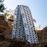 A pair of MAXTRAX XTREME / White Limited Edition, shown standing upright in a dirt slope outdoors under a clear blue sky.