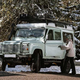 Vintage Land Rover Defender in a snowy forest setting with a person opening the door.