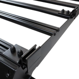 Close-up of a Front Runner Series Slimsport Side Mount Accessory Bracket / Small mounted to a black metal roof rack frame with parallel mounting rails and bolted brackets on a white background.