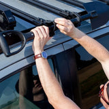 Close-up of a person's hands installing a spade to a black roof rack  using the Front Runner Series Slimsport Side Mount Accessory Bracket / Small, in bright daylight.