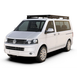 A white Volkswagen Transporter van with a black Front Runner Volkswagen T5 Transporter SWB (2003-2015) Slimline II Roof Rack Kit, shown from a three-quarter front angle on a solid white background.