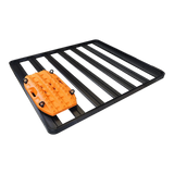 A black metal roof rack with multiple parallel slats and a Front Runner Series Recovery Device Mounting Kit, used to mount an orange Maxtrax Recovery Device, shown on a plain white background.