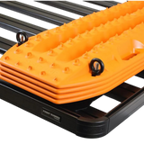 Bright orange Recovery Device with raised grip spikes and a black Front Runner Series Recovery Device Mounting Kit, shown mounted on a black roof rack frame.