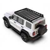 A white SUV shown from a three-quarters rear angle on a light gray studio background, fitted with a black Front Runner GWM Tank 300 (2023-Current) Slimline II Roof Rack Kit and rear spare tire.