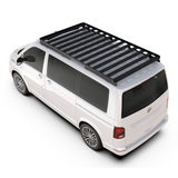 A white Volkswagen van shown from an elevated rear-left angle on a clean white background, fitted with a black Front Runner Volkswagen T6/T6.1 Caravelle Transporter SWB (2015-Current) Slimline II Roof Rack Kit.