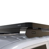 A black Front Runner Volkswagen T6/T6.1 Caravelle Transporter SWB (2015-Current) Slimline II Roof Rack Kit mounted to a silver vehicle roof, featuring a front bumper mount and a small 'FRONT BUNNER' brand badge.