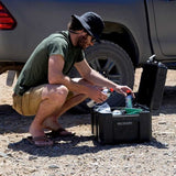 Person crouched next to a Camp 4x4 Rentals vehicle with a Front Runner Wolf Pack Pro Hi-Lid Ammo Box in a desert landscape