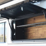 Open Front Runner Land Rover Defender (1983-2016) Gullwing Window with a wood-paneled interior and metal shelf, attached to a white vehicle.