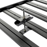 A close-up of a Front Runner Series Spare Wheel Clamp, a black metal roof rack mounting bracket with a wingtip screw and adjustment wing, shown attached to parallel roof rails on a white background.