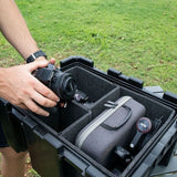 Person placing a camera into a Front Runner ammo box with Storage Box Foam Dividers in a Wolf Pack Pro on a white background