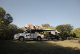 Camper truck with Front Runner rooftop tent parked in a grassy area with trees