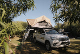 White Toyota Hilux with a rooftop tent parked in a forested area.