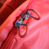 Close-up of a bright coral-pink 120lt MEERKAT Travel bag with a matching zip closure and dual zipper pulls featuring dark blue braided cords and pink rubber loops.