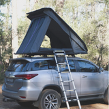 RoofPod Rooftop tent on a silver SUV with ladder in a forest setting