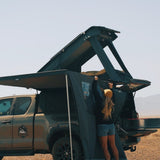 Person standing next to a truck with an open RoofPod roof tent in a desert setting