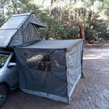 RoofPod Awning with the awning sides and door erected and attached to a vehicle in a forest setting
