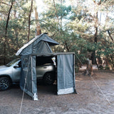 RoofPod Awning with the awning sides and door erected and attached to a vehicle in a forest setting