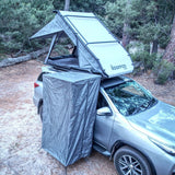 Car with a rooftop tent and a RoofPod Shower/Privacy Cube attached in a forest setting